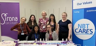 A group of staff from NBT, UHBW and Sirona people standing behind a table at the Deaf and Hard of Hearing Information Day