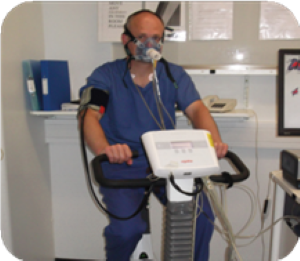 Person sitting on exercise bike wearing mask and blood pressure cuff for cardiopulmonary exercise test