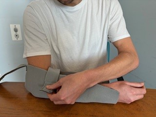 Person with arm in polysling trough, resting on table, fastening strap near elbow