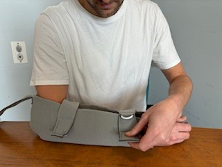 Person with arm in polysling, resting on table, fastening strap near wrist