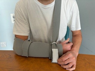 Person with arm in polysling, resting arm on table, adjusting shoulder strap through D rink attached to trough