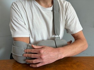 Person wearing polysling attaching waist strap to elbow end of trough