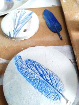 Some art work of blue and white leaf imprints on a white surface with a blue feather in the background