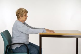 Woman sitting up straight at table with arms stretch and hands face down