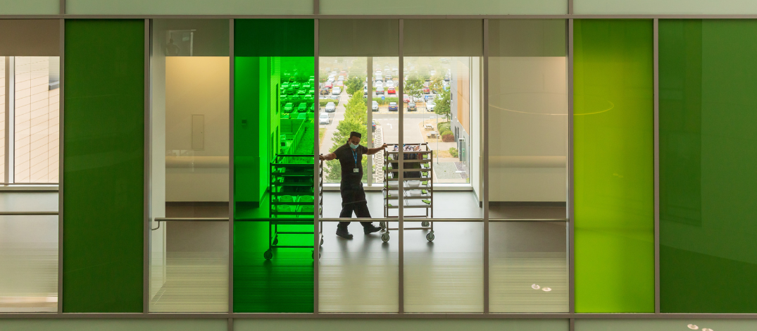 A staff member wheels trollies down a corridor with windows looking into the atrium and the outside.