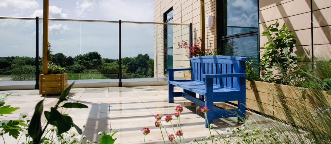 The ICU rooftop garden with a blue bench looking out onto a green view with flowers around it.