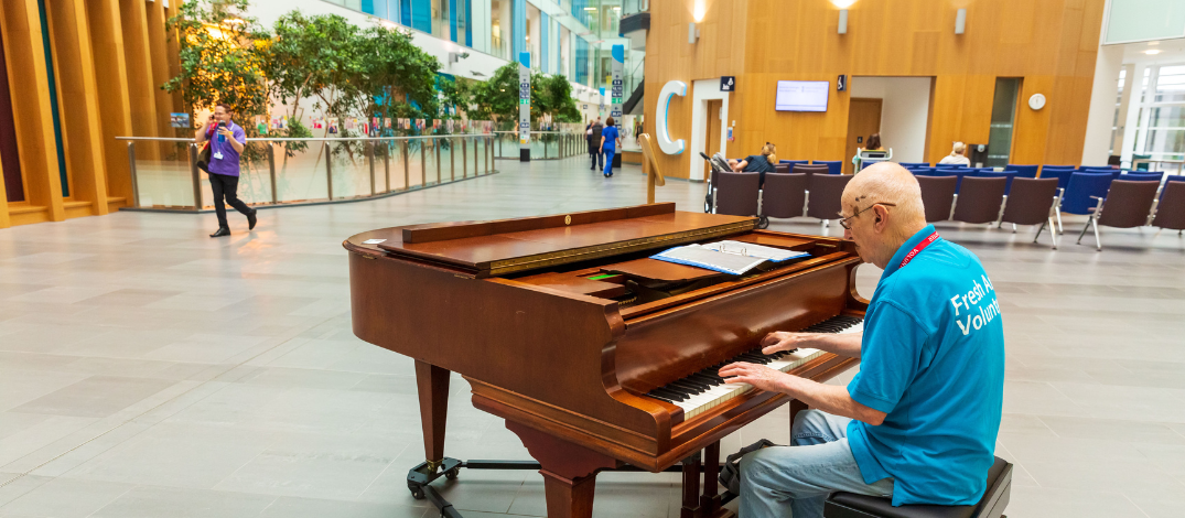 A volunteer musician plays the piano in the Brunel atrium.