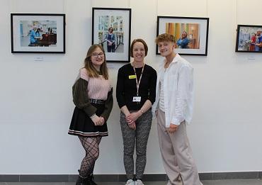 Three people sat together in front of framed photographs