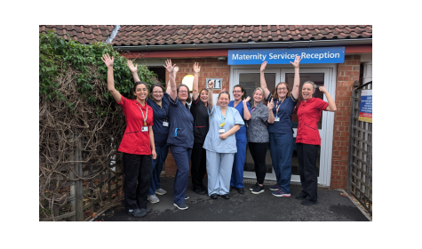 Nine women celebrate with their hands up outside a building