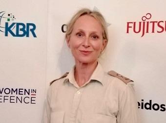 Woman wearing military uniform stood in front of backdrop wit branding including "Women in Defence".