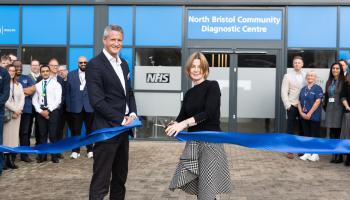 Two people stand in the forefront, cutting a blue ribbon. Behind them is a building with a sign above the door reading "North Bristol Community Diagnostic Centre"