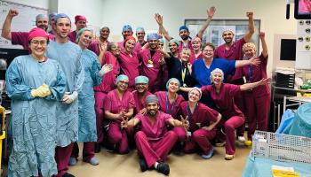 Surgeons in pink scrubs pose as a group inside an operating theatre