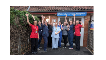 Nine women celebrate with their hands up outside a building