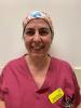 Woman in raspberry-coloured scrubs and a theatre cap looking at the camera, smiling